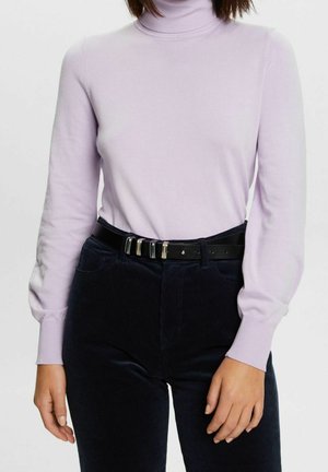 Femme portant un pull à col roulé violet clair rentré dans un pantalon taille haute bleu marine foncé avec une ceinture noire.