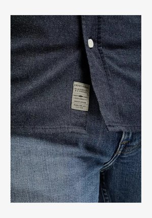 Ciemnoniebieska koszula dżinsowa z zapięciem na guziki, z metką "CROSS JEANS" oraz połączeniem ciemnych i jasnych tekstur denimu.