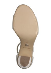 Sandale à talons hauts avec une semelle lisse couleur hâlée, des accents métalliques et une sangle beige. Présente une texture pour une meilleure adhérence et un détail de logo circulaire sur la semelle.