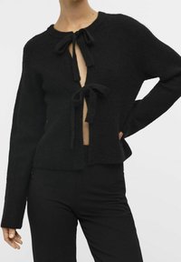 Cardigan noir tricoté à manches longues, devant ouvert avec deux nœuds, texture côtelée et coupe courte.