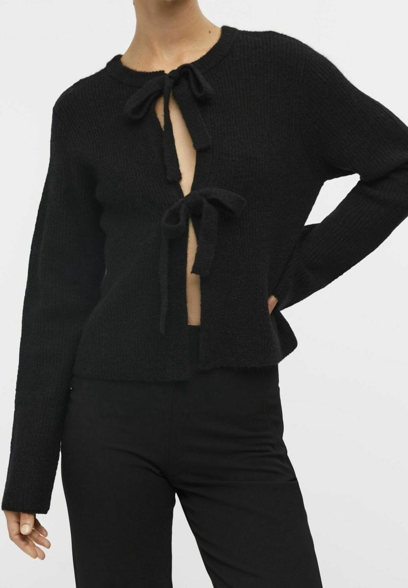 Cardigan noir tricoté à manches longues, devant ouvert avec deux nœuds, texture côtelée et coupe courte.