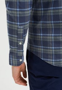 Pánská kostkovaná košile v námořnické modři, zelené a světle modré barvě, vyrobená z měkké látky. Má knoflíkové manžety a zakulacený spodní lem.