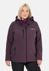 Chaqueta softshell morada con capucha, bolsillos con cremallera y un logo. Presenta una textura suave y un diseño ajustado con elementos ajustables.