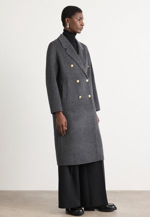 Gray houndstooth double-breasted coat with gold buttons, side pockets, and long sleeves, worn over black wide-leg pants and a turtleneck.