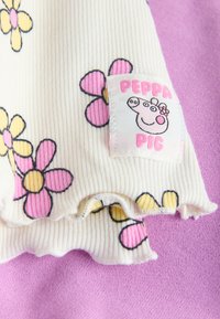 Tela blanca acanalada con flores de dibujos animados rosas y amarillas y un parche de Peppa Pig sobre un fondo textil púrpura.