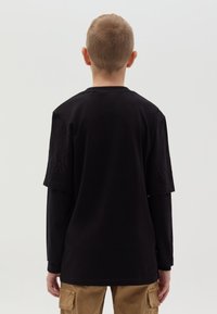 Zwarte katoenen t-shirt met korte mouwen, met subtiele vlam borduursels op de schouders. Gedragen over een lange mouw shirt met een losse pasvorm.