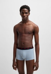 Light blue boxer shorts with a black waistband featuring red "HUGO" logo. Soft fabric, fitted design, and mid-thigh cut.