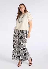Beżowy top z krótkim rękawem zestawiony z czarnymi spodniami w szerokim kroju z białym wzorem w liście palmowe. Uzupełniony geometrycznym naszyjnikiem i czarnymi szpilkami.