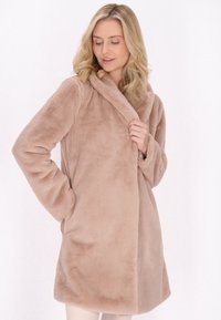 Cappotto in pelliccia sintetica di un morbido beige, con colletto ampio, maniche lunghe e tasche laterali. Texture liscia e design lungo fino al ginocchio.