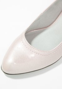 Vaaleanpunaiset kiiltävät kengät, joissa on terävä kärki, teksturoitu pinta ja pehmeä harmaa sisempi. Yksityiskohtana on hillitty tikkaus yläreunassa.