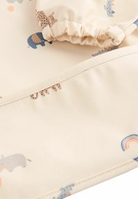 Tessuto resistente all'acqua con uno sfondo crema caratterizzato da motivi di animali colorati e accenti arcobaleno; dettaglio di polsini arricciati.