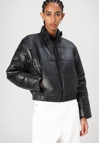 Svart puffjakke med cropped design, med ståkrage, quiltet tekstur og elastisk kant. Glidelås foran og sidelommer.