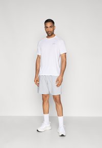 White short-sleeve athletic shirt and light gray shorts, paired with white sneakers and ankle socks, standing on a neutral background.