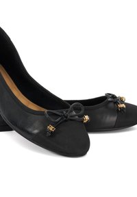 Black ballet flats with a rounded toe, featuring a textured finish, small bows, and gold accents on the front. Low, sturdy heel.