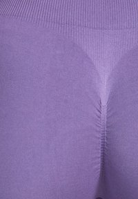 Primer plano de tela morada sin costuras de talle alto que muestra una cinturilla texturizada y un detalle de costura central fruncida.