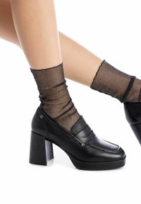 Mocassini neri con plateau e tacco spesso, con una finitura in pelle liscia e dettagli laterali, abbinati a una calza trasparente nera a trama.