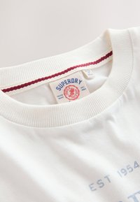 Nærbillede af hvid crew neck t-shirt krave med rød stingdetalje og Superdry mærkat indeni.