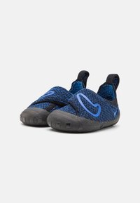 Kék és fekete sportcipők texturált kötött felsőrésszel, slip-on kialakítással, fekete gumitalppal és kék díszítéssel az oldalakon.