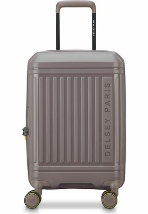 Maleta gris de carcasa dura con ranuras verticales, asa retráctil, cuatro ruedas giratorias y la marca "DELSEY PARIS" en el frente y el asa.