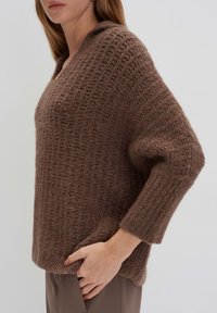 Brauner Strickpullover mit strukturiertem Gewebe, lockerer Passform und überschnittenen Schultern. Besitzt einen V-Ausschnitt und lange, weite Ärmel.