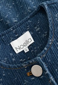 Camicia in denim con trattamento blu e un motivo sottile, colletto rotondo, bottone a pressione in metallo e etichetta con scritto "Noella, S."