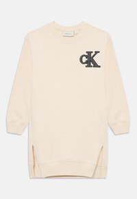 Ljusbeige sweatshirt med långa ärmar, sidöppningar och en texturerad svart "ck"-logotyp på vänster bröst. Mjuk bomullsmaterial.