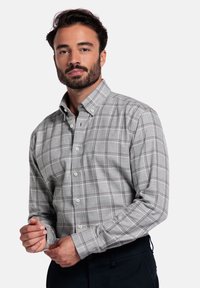 Grijze geruite blouse van stof, met een button-down kraag, lange mouwen en witte knopen. Subtiele contrasterende oranje en blauwe lijnen.