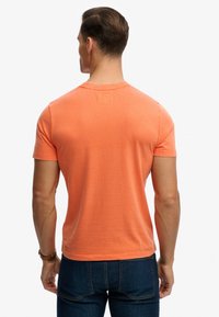 Short-sleeve, crew-neck t-shirt in bright orange cotton, featuring a small rectangular tag at the neckline, with a smooth texture.