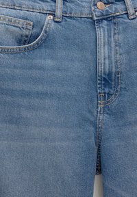Jeans de denim azul claro con un diseño clásico de cinco bolsillos, cierre de botón metálico y costuras visibles. Textura suave con áreas descoloridas.