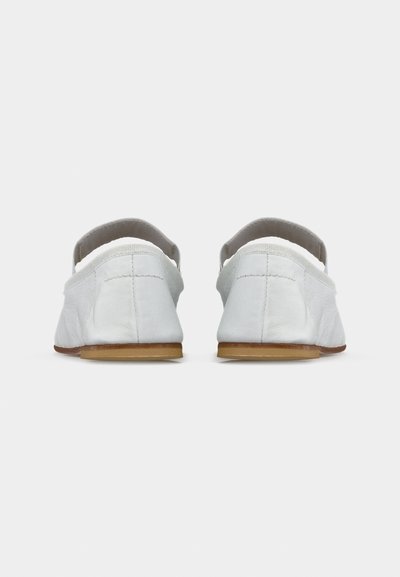 Ζευγάρι λευκές δερμάτινες μπαλαρίνες με ελαστικούς ιμάντες, ορατές από πίσω σε απλό φωτεινό φόντο.