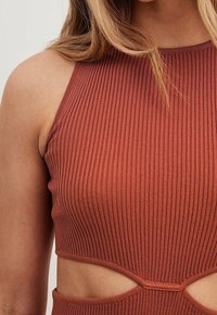 Haut halter côtelé de couleur rouille avec des découpes, présentant un design ajusté et une texture lisse, mettant en valeur des côtés ouverts pour un style supplémentaire.