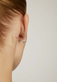 Pendiente de aro plateado con acentos puntiagudos visibles desde atrás. Acabado metálico liso, usado en la parte inferior de la oreja. Diseño minimalista.