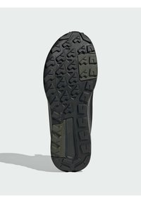 Schwarze Gummisohle mit einem strukturierten, robusten Profil. Enthält erhabene geometrische Formen für Traktion und einen leichten grünen Akzent.