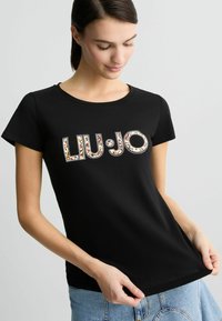 Juodas medvilnės marškinėliai su prigludusia išvaizda, apvaliu iškirpimu ir "LIU JO" logotipu, papuoštu spalvingomis akmenimis ir blizgučiais.