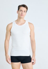 Débardeur blanc avec un col rond et de larges bretelles, associé à des boxers noirs. Texture lisse, design simple.