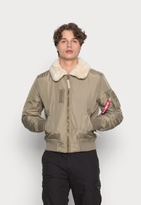 Chaqueta bomber en satin verde oliva con un cuello de piel sintética crema, puños y dobladillo acanalados, con cinturón frontal y bolsillos laterales.