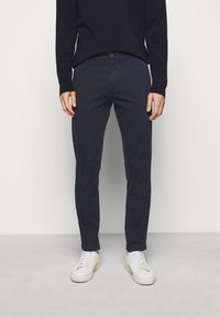 Granatowe bawełniane chinosy o slim fit, z przednimi kieszeniami i zapięciem na guzik, zestawione z białymi trampkami.