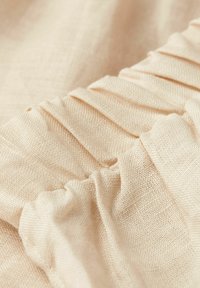 Tela color champán con textura suave, que presenta plisados a lo largo de un borde, creando un sutil interés visual y profundidad.