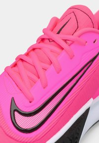 Atletické boty Nike v jasně růžové barvě, s texturovaným syntetickým svrškem, silnými růžovými tkaničkami, výrazným černým logem Swoosh a vzorovanými detaily.