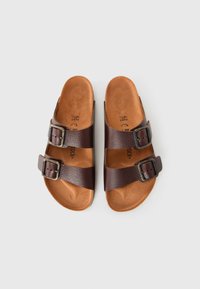 Két állítható csattal ellátott barna bőrszandál, világosbarna talppal, fehér háttér előtt, felülről nézve.