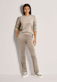 Beiges Veloursoberteil mit dezentem Leopardenmuster und langen Ärmeln, kombiniert mit passenden beigen Velourshosen und strukturierten Sneakers.