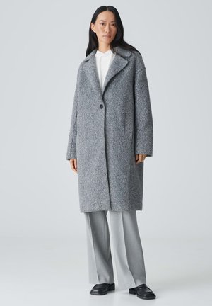 Gray wool coat with a notched collar, single button closure, and side pockets, paired with gray trousers and black shoes.