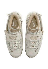 Vita Nike-sneakers med ett beige rem, texturerade ytor och snörningsdesign. "Nike"-loggan och "Air"-märket synliga inuti.