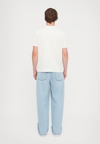 Light beige short-sleeve t-shirt with a round neckline, paired with loose-fitting light blue jeans featuring back pockets.