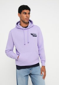 Lila kapucnis pulóver puha anyagból, elülső zsebbel, húzózsinórral ellátott kapucnival és fekete "Tommy Jeans" logóval a mellrészen.