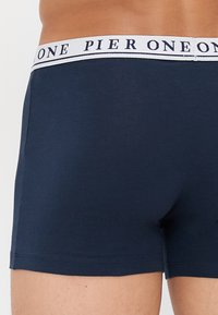 Tamno plave pamučne bokserice s bijelim pojasom na kojem je otisnuto "PIER ONE". Glatka tekstura, prilagođen dizajn, kratka dužina nogavica.