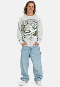 Grijze sweatshirt met een grafische print en de tekst "DC Athletics," gecombineerd met lichtblauwe baggy jeans en witte schoenen.