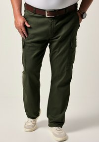 Pantalones cargo verde oliva con corte recto, cierre de botón y dos bolsillos laterales. Llevados con una camiseta blanca y zapatillas de color claro.