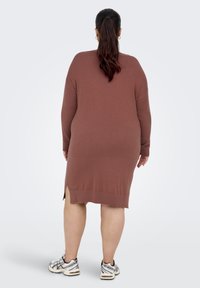 Bruine gebreide jurk met lange mouwen, zijsplitten, midi-dij lengte en een ontspannen pasvorm, gecombineerd met witte en zilveren sportschoenen.