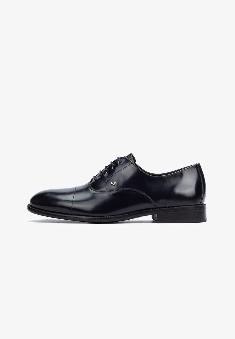 Elegante scarpa da uomo in pelle nera lucida Oxford con allacciatura chiusa, punta tonda, tacco basso e piccolo logo argentato sul lato.